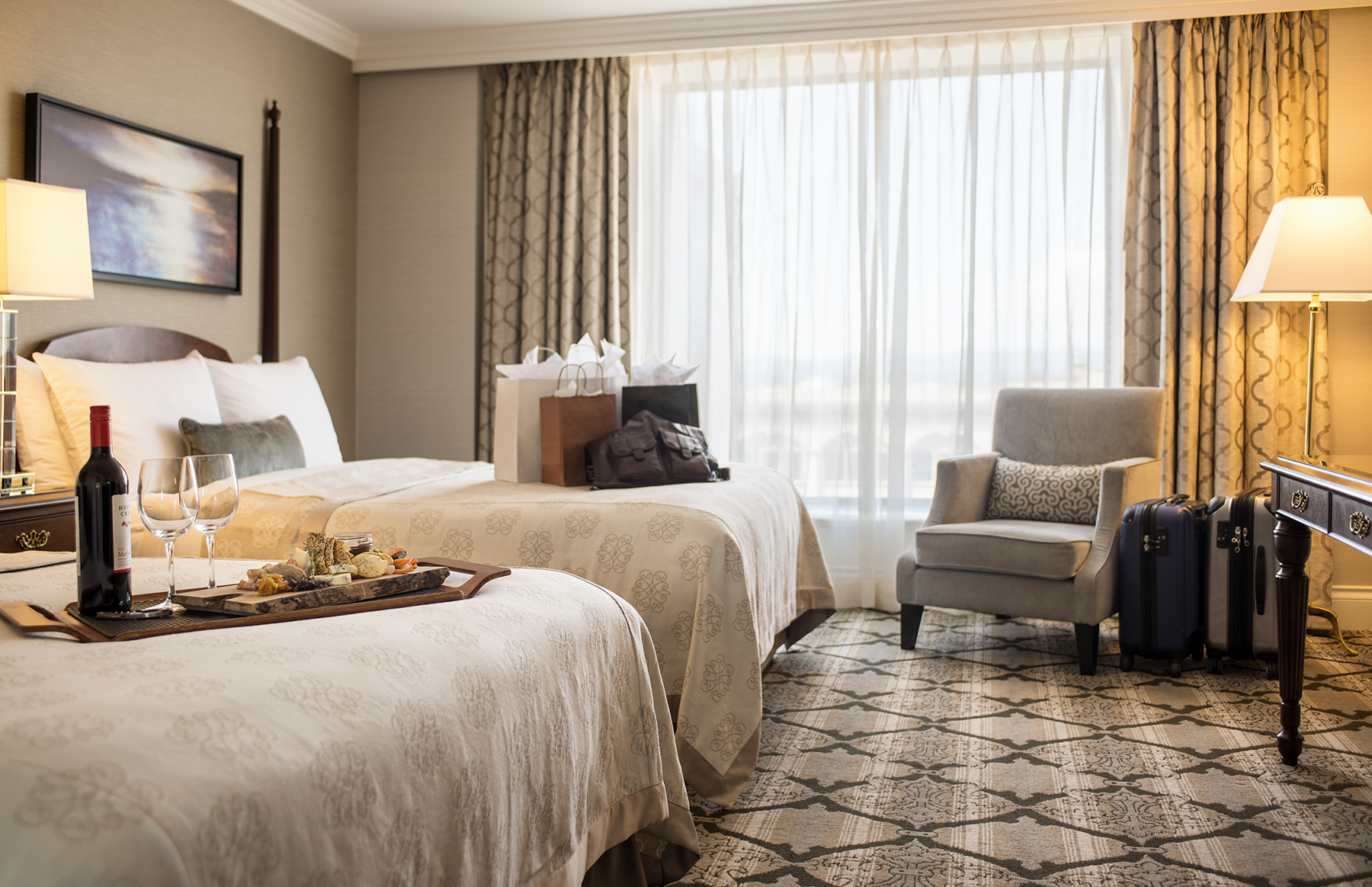 Two queen beds in brightly lit room with floor to ceiling windows. Ornate carpets and cozy bedding with a white orchid on table by window.